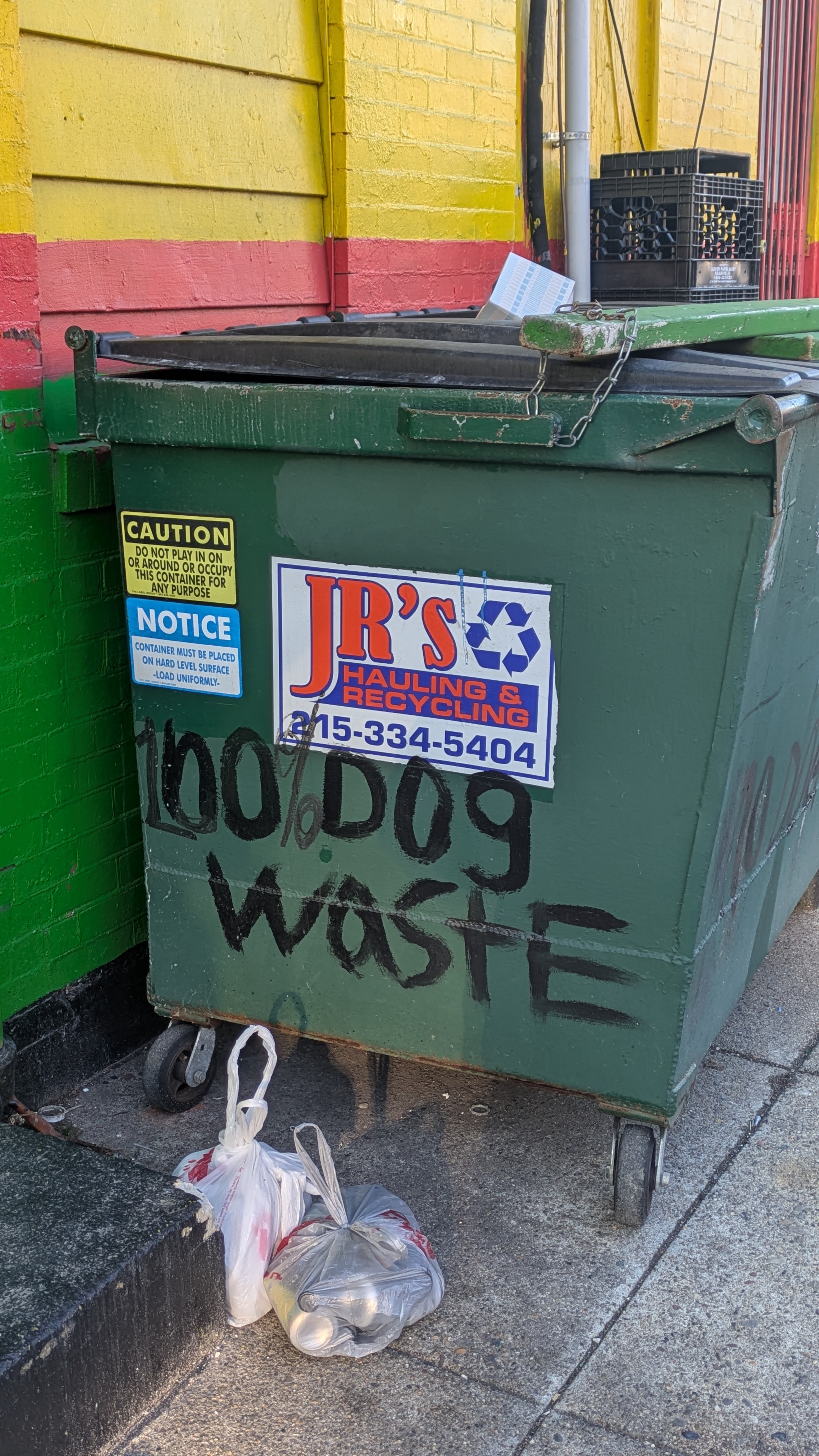 Photograph of a dumpster that has text scrawled on it in black paint. The text clearly used to read: no dog waste. In all lowercase letters. However, someone used more black paint to make it read: One-hundred percent dog waste.