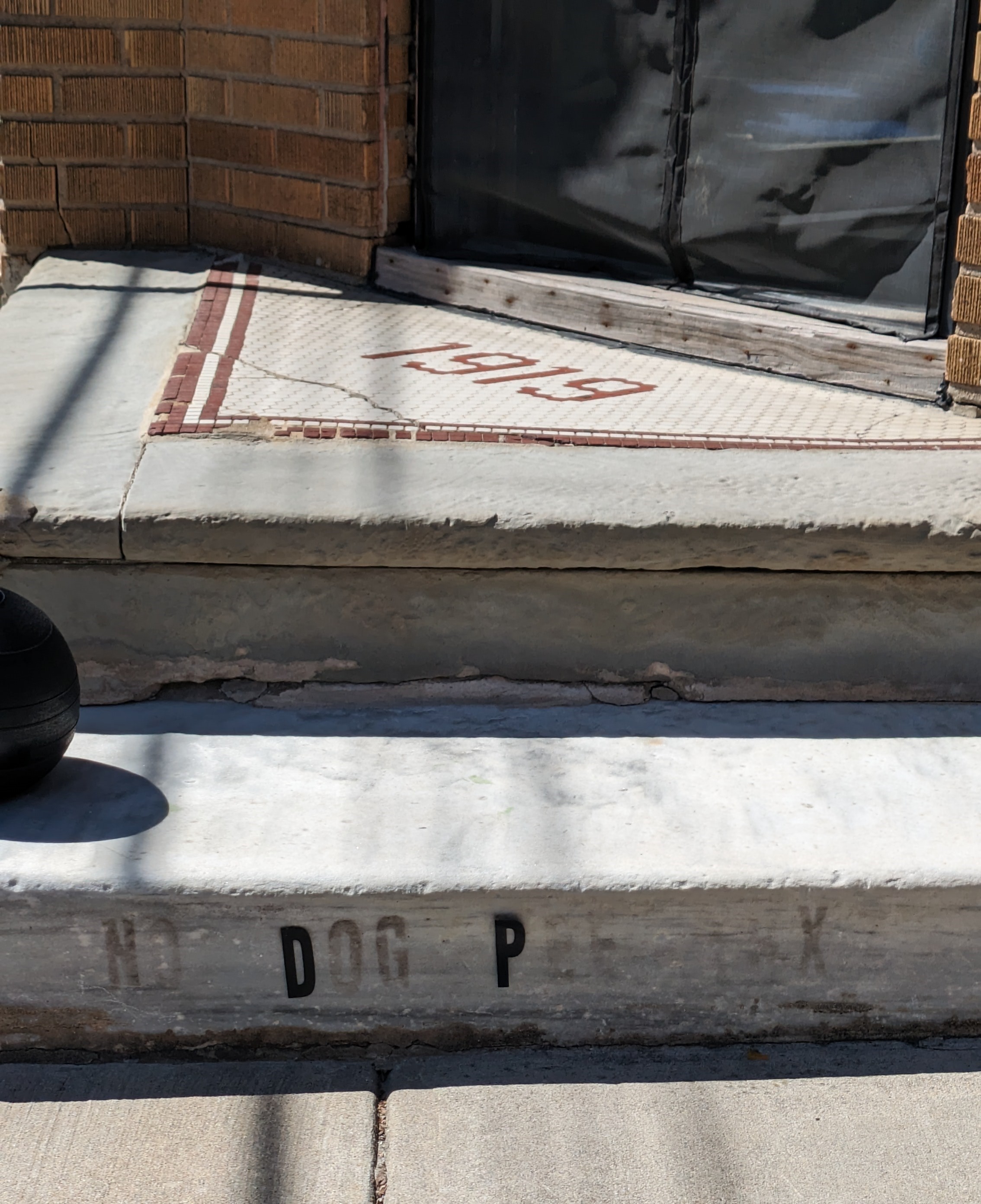 Photograph of stone steps with all caps black vinyl lettering stickers on the lowest step. Most of the lettering has fallen off, but the glue remains so you can still make out that it once read NO DOG PEE THX. Only the letter D in dog and the letter P in pee stickers still remain.